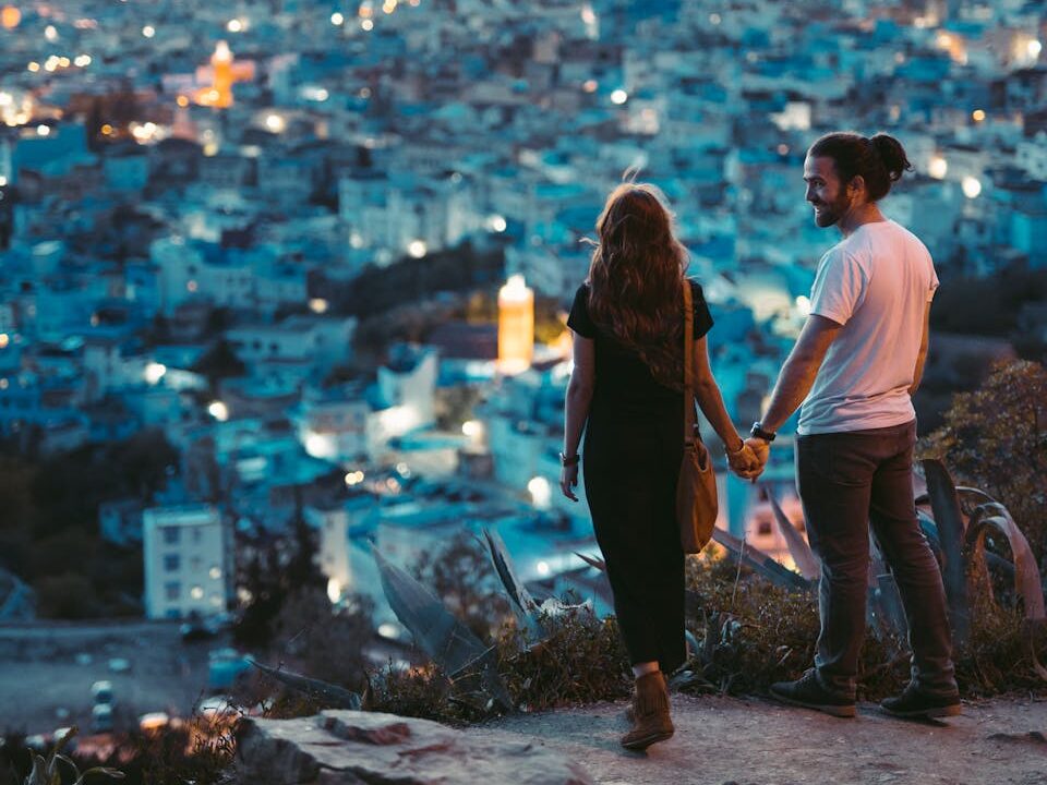A romantic couple holding hands with a view of Chefchaouen, Morocco at twilight.
