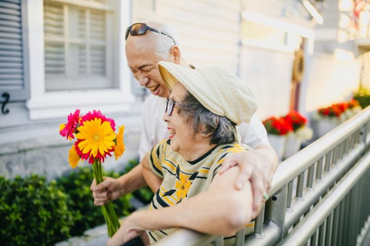 Asian elderly couple holding flowers and smiling together outdoors.