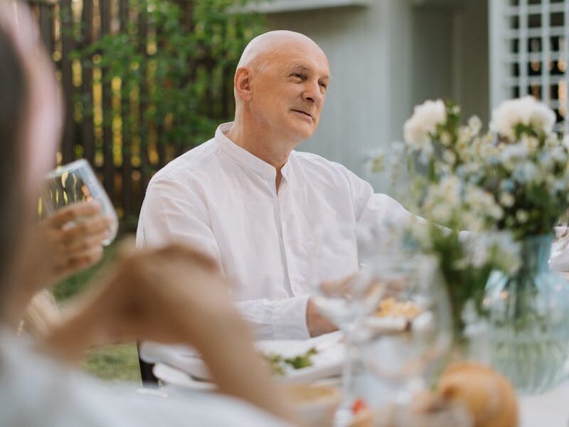 Senior man enjoys a serene outdoor dinner surrounded by friends and nature.