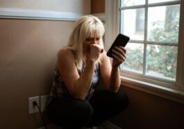 Woman sitting in deep thought by a window, holding a smartphone.