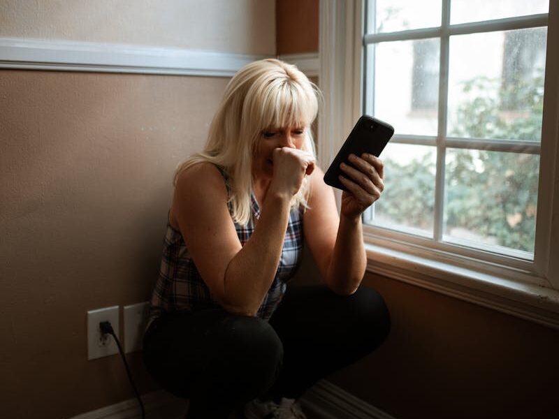 Woman sitting in deep thought by a window, holding a smartphone.
