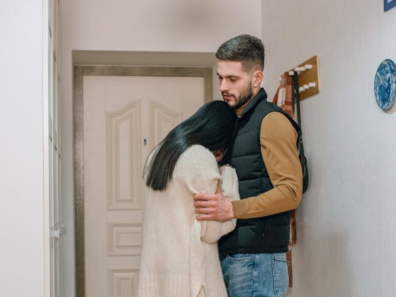 An emotional couple embraces in a hallway, conveying sadness and comfort at home.