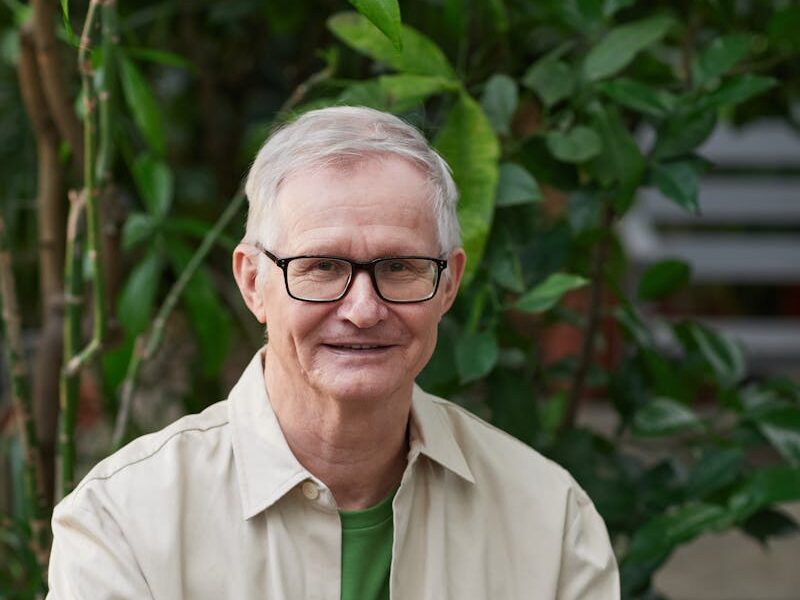 Elderly man enjoying remote work on a laptop in a garden setting.