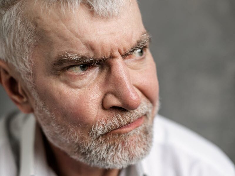 Portrait of a senior man with grey hair, looking pensive and serious, dressed in white shirt.