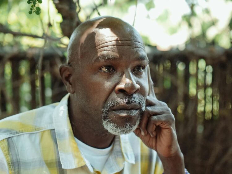 A senior African American man deep in thought, sitting outdoors on a sunny day.