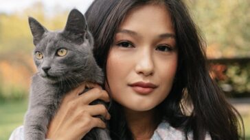 A young woman holds a gray cat outdoors in a serene setting, showcasing companionship and beauty.