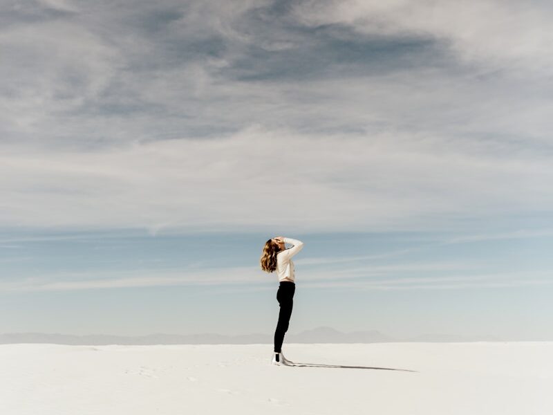 woman looking up to the sky while standing on white sand