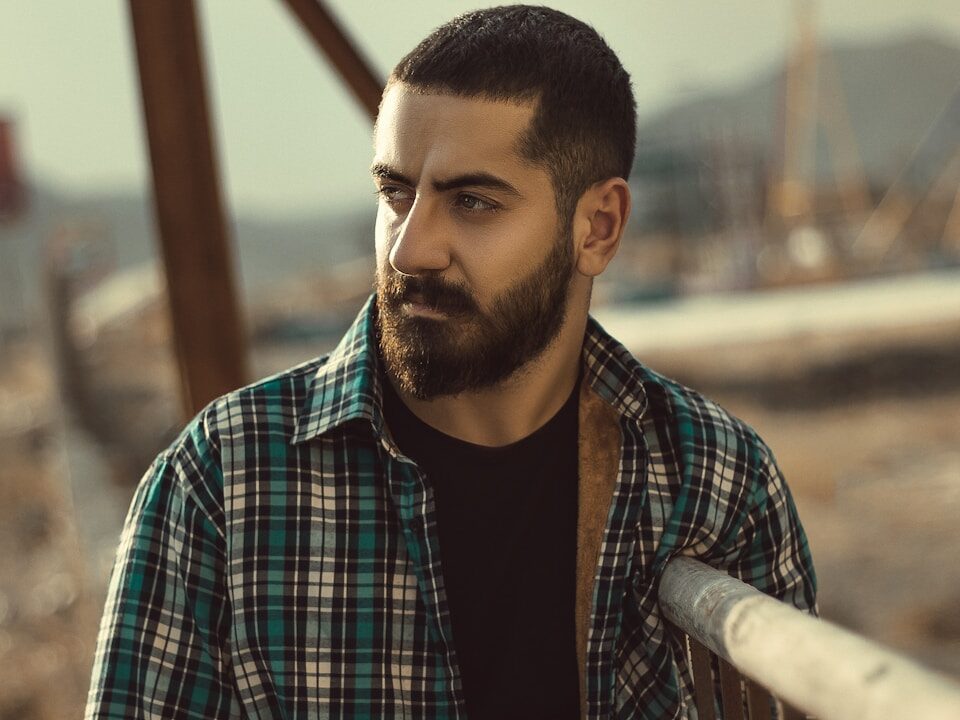 man in black and white plaid dress shirt standing near brown wooden railings during daytime