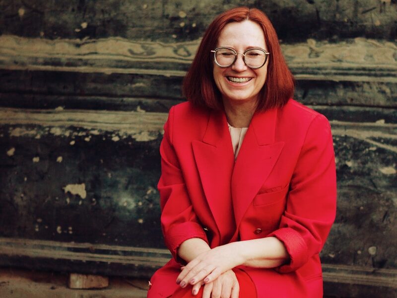 woman in red blazer and black skirt sitting on brown concrete stairs