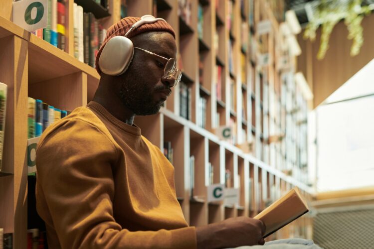 A man reads a book surrounded by bookshelves.