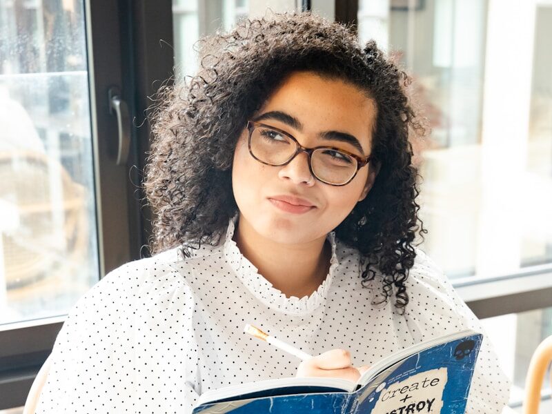 woman in white and black polka dot shirt holding blue and white book