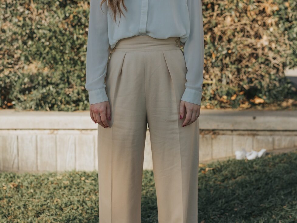 woman wearing gray button-up long-sleeved shirt and brown pants standing in front of bushes