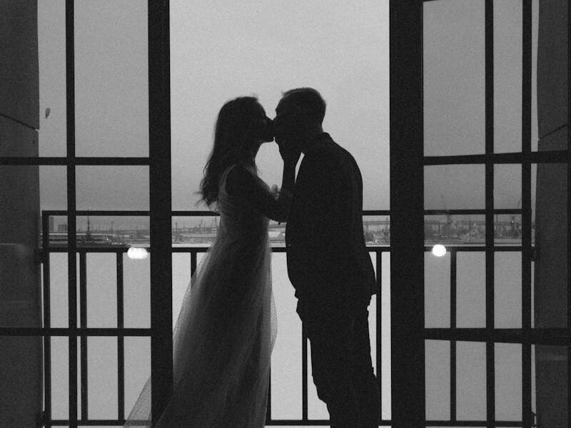 Black and white silhouette of a couple sharing a romantic kiss on a balcony during their wedding.