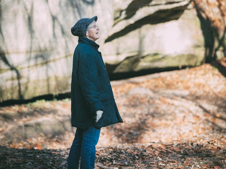 A senior woman in a jacket walking through a leafy autumn landscape.