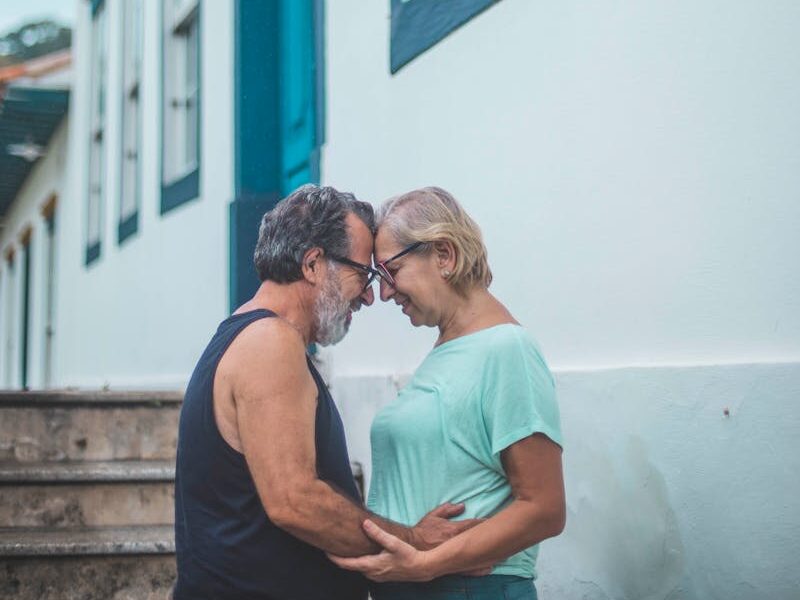 Senior couple sharing a tender moment outdoors by a blue and white house.