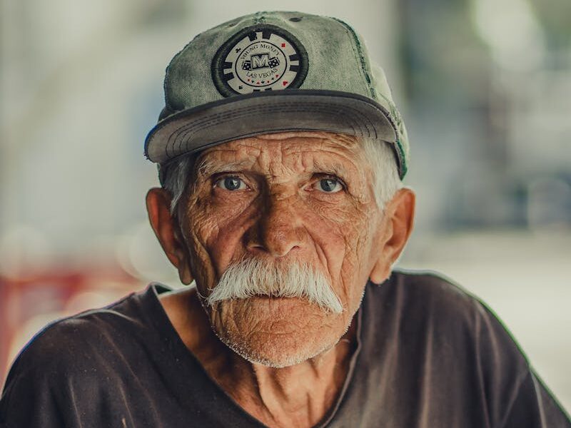 Portrait of an elderly man with a mustache, wearing a cap and serious expression, outdoors.