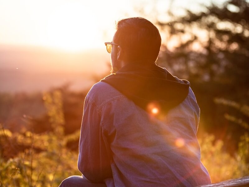 woman in white shirt and sunglasses sitting on brown wooden bench during sunset