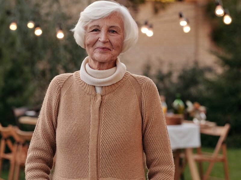 Cheerful senior woman in a cozy cardigan enjoying an outdoor gathering in the garden.