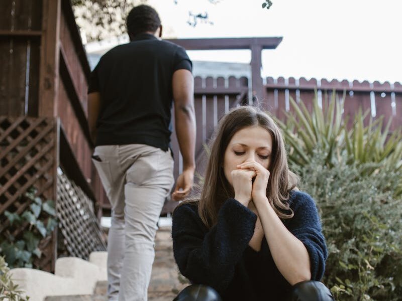A woman sitting in distress while a man walks away outdoors, capturing emotion and separation.