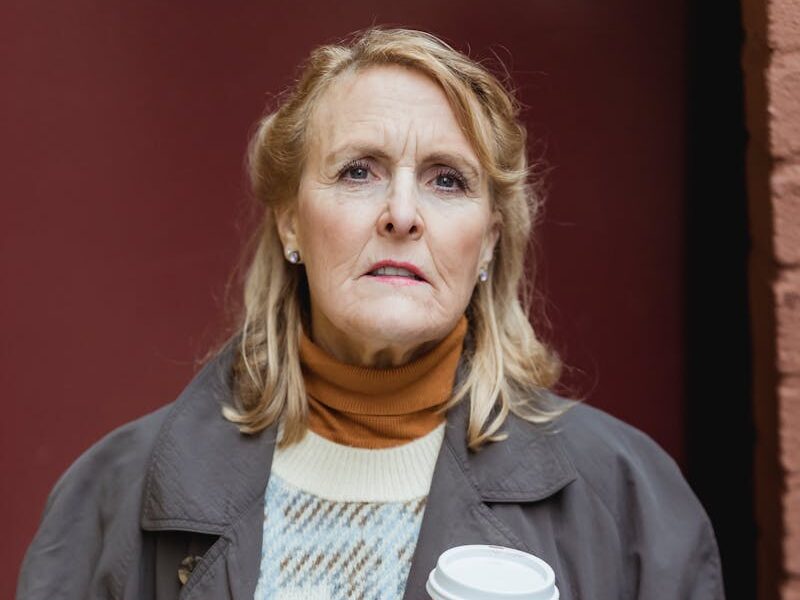 Senior woman in warm clothes holding a coffee cup outdoors on a cool day.