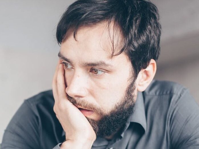 A worried man in a gray shirt holds a credit card, symbolizing online fraud or financial stress.