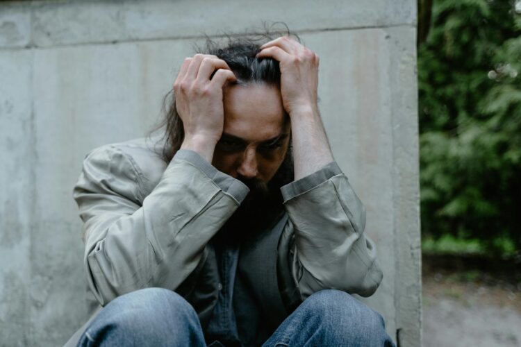 A pensive man sitting outdoors, expressing deep contemplation and emotional struggle.