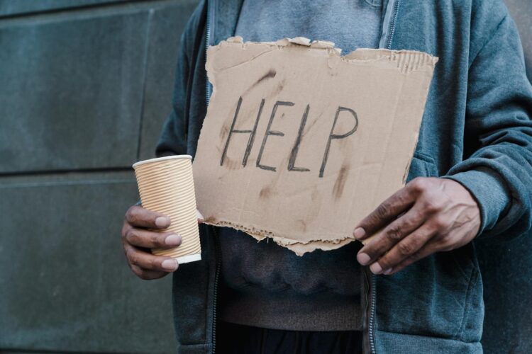 Close-up of a person holding a cardboard sign with 'Help' and a paper cup, representing need and assistance.