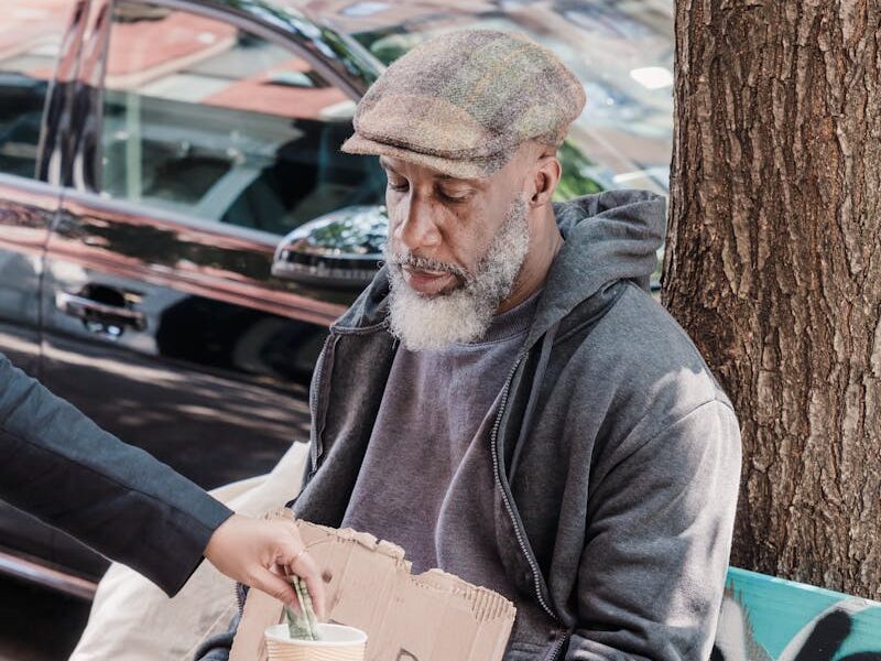 An elderly man seated on a bench receives money in an urban setting.