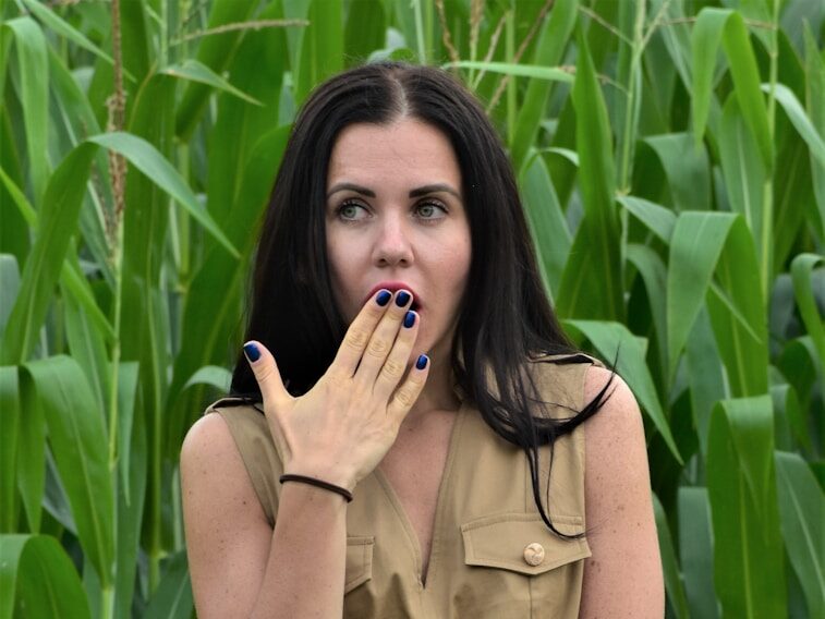 a woman standing in a field with her hands in her mouth