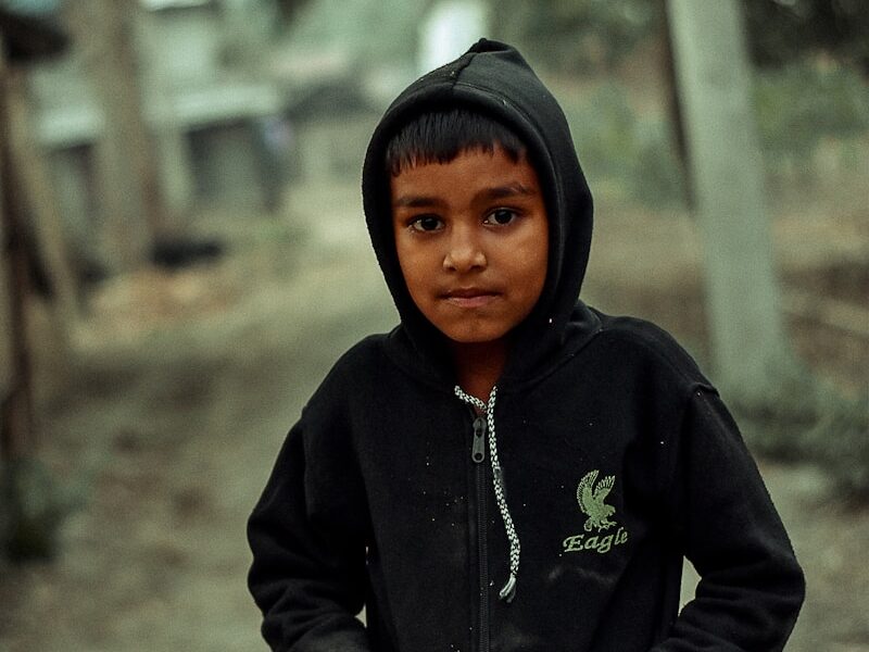 a young boy in a black hoodie standing on a dirt road