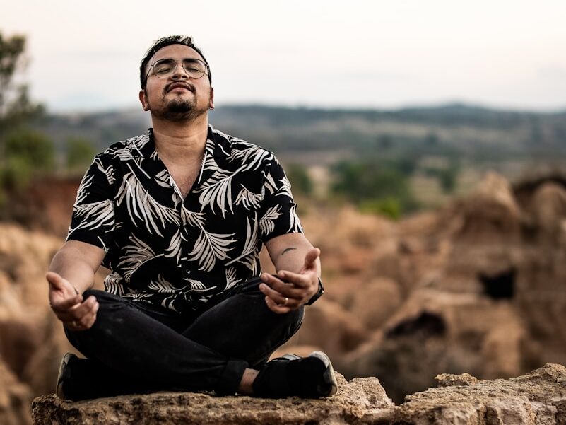 man in black and white floral dress shirt sitting on brown rock during daytime