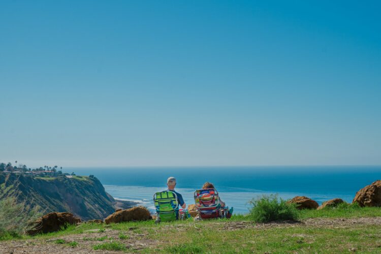 2 person sitting on green grass field near body of water during daytime