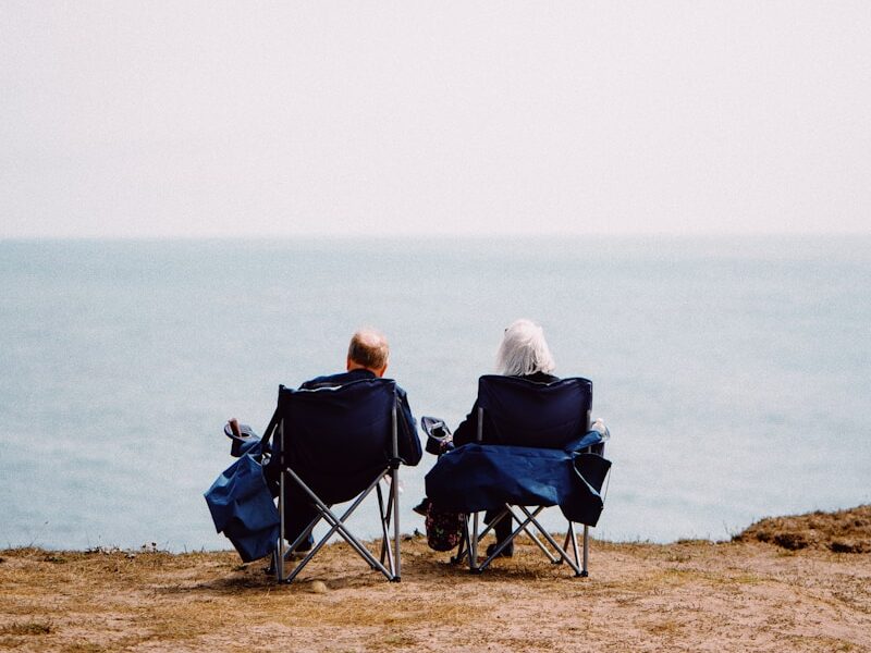 2 person sitting on blue camping chairs on brown field during daytime