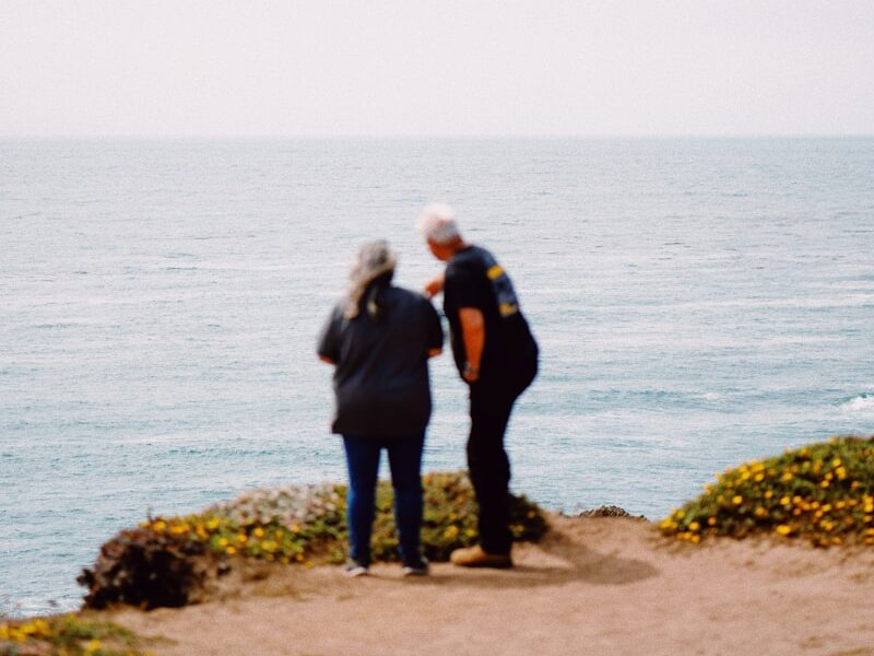 man and woman standing on rock near body of water during daytime