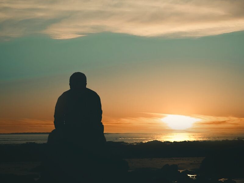 silhouette of man standing on seashore during sunset