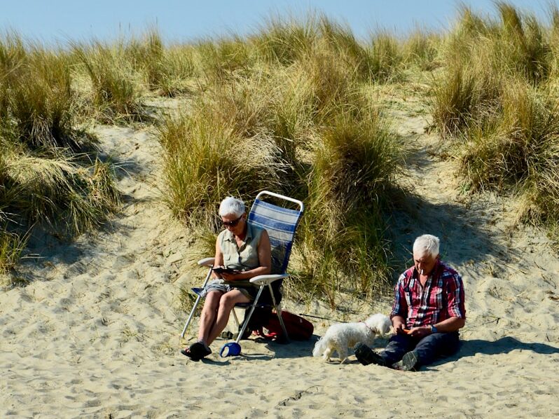 man in red and white jacket sitting on red and black chair on white sand during