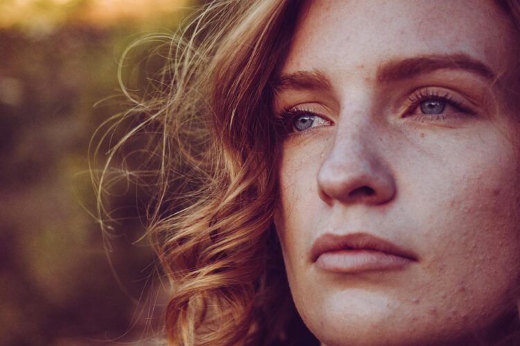 Close-up portrait of a young woman with curly hair and blue eyes, exuding calmness.
