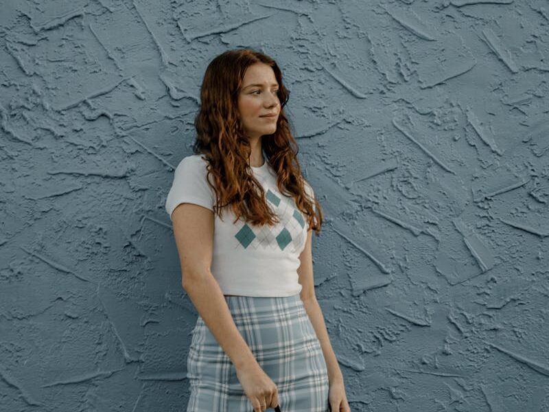 A fashionable woman stands confidently against a blue textured wall, showcasing summer style.