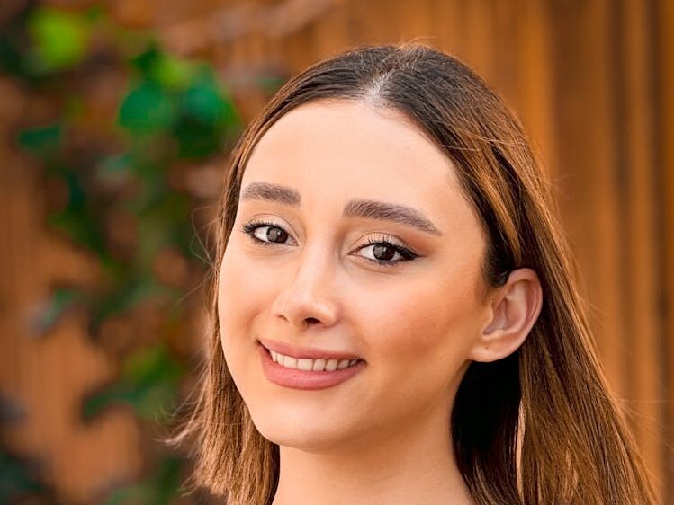 Portrait of a smiling woman in Muscat, Oman, wearing a black shirt against a warm outdoor backdrop.