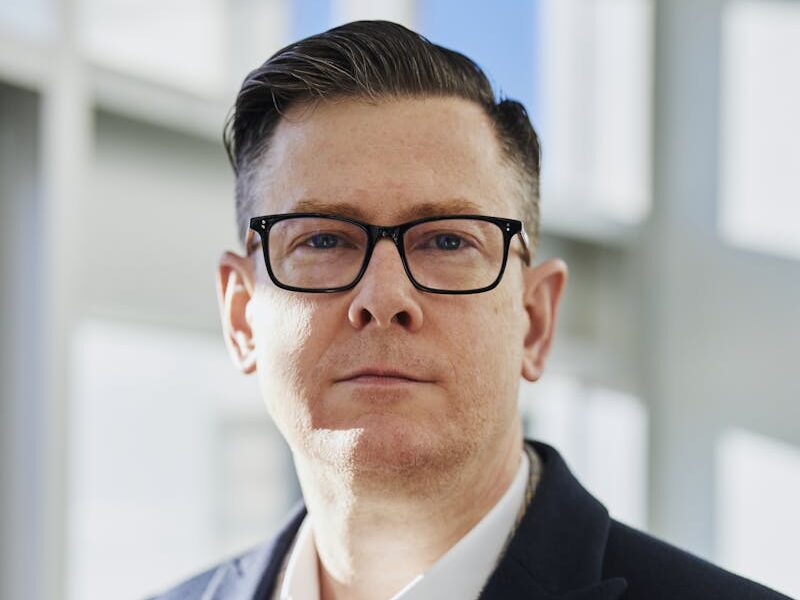 Profile portrait of a confident business executive wearing eyeglasses in a sunlit office setting.