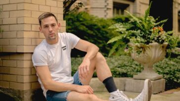 Young man in casual wear sitting on pavement outdoors, Chicago suburb vibe.