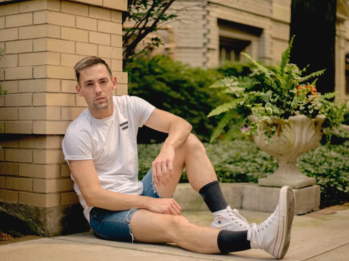 Young man in casual wear sitting on pavement outdoors, Chicago suburb vibe.