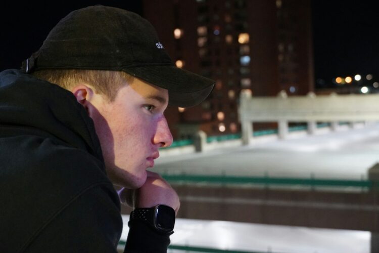 a man in a black jacket and hat looking off into the distance