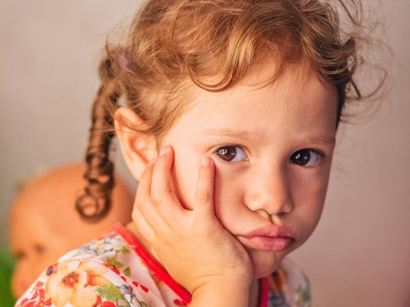Charming portrait of a thoughtful toddler in a colorful floral dress indoors.