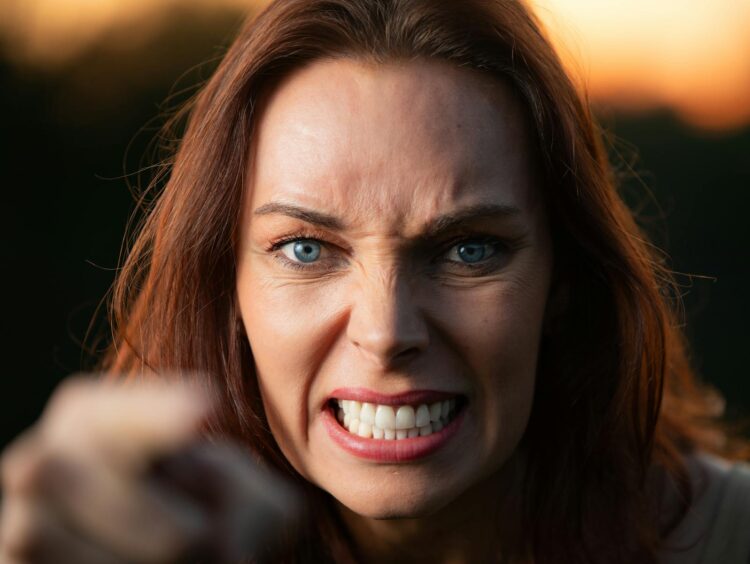 Close-up of a woman showing strong anger with clenched teeth and intense gaze outdoors.