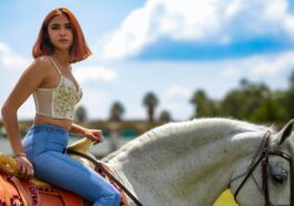 A young woman rides a white horse outdoors, enjoying a sunny day with clear skies.