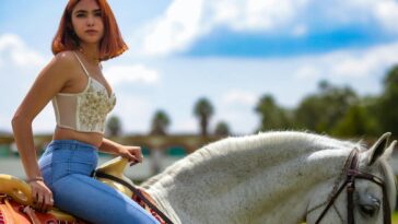 A young woman rides a white horse outdoors, enjoying a sunny day with clear skies.