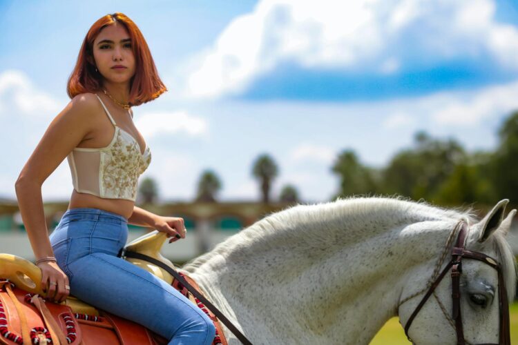 A young woman rides a white horse outdoors, enjoying a sunny day with clear skies.