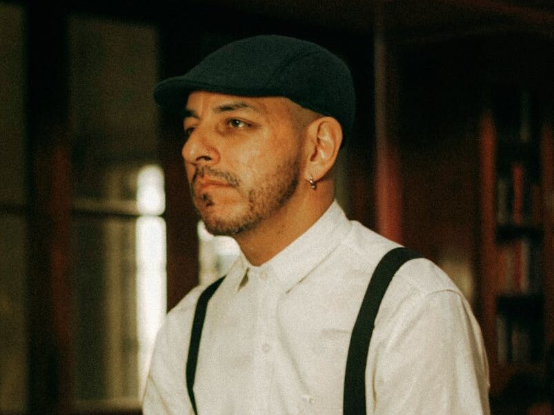 Vintage-styled portrait of a man in suspenders and flat cap indoors.