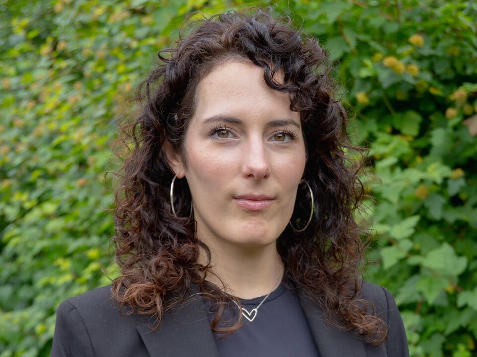 Confident woman with curly hair posing in a black suit outdoors.